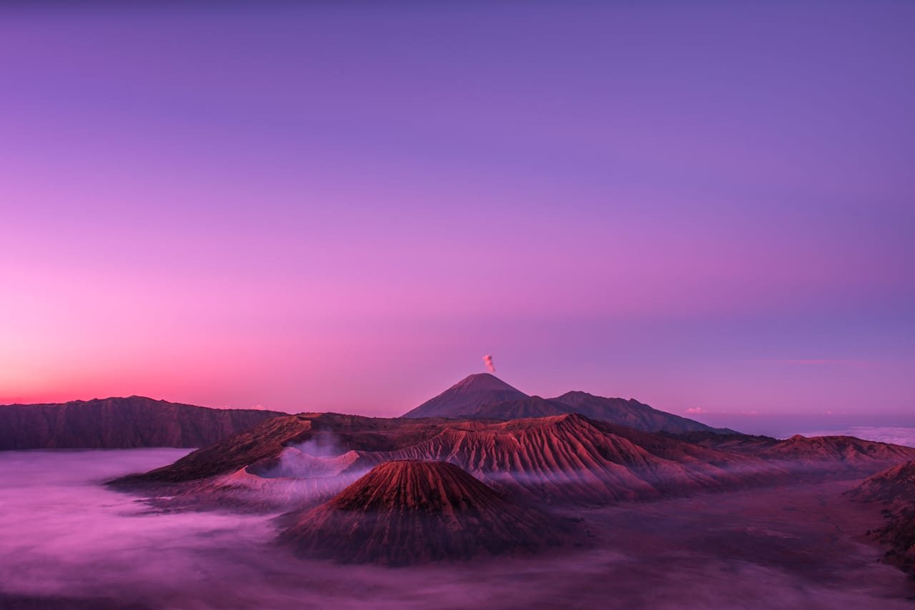火山口在第一道晨光里，云海与天空呈品红与紫色。