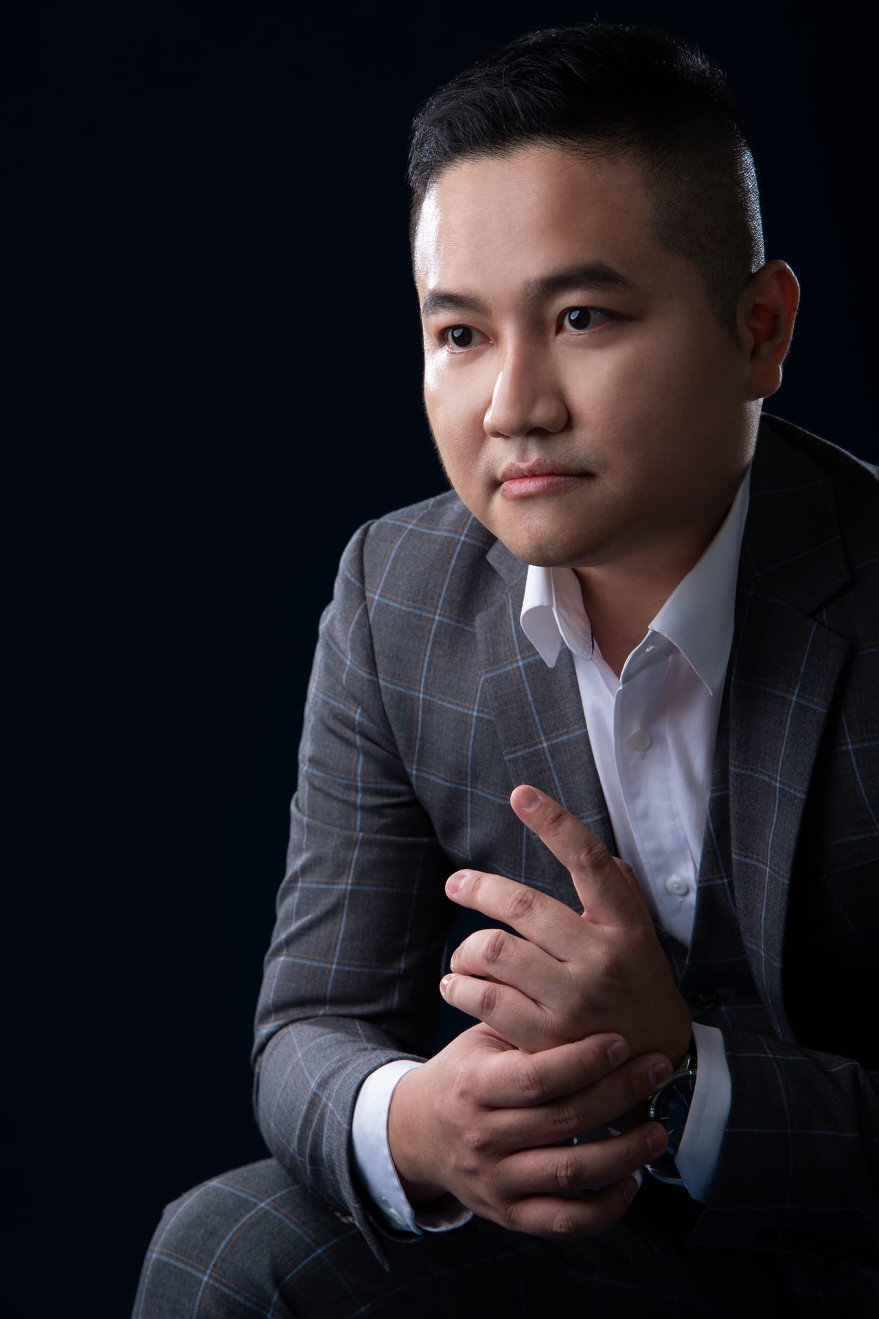 Against a deep-blue background, Kevin sits with his hands lightly clasped, looking attentively at the camera.