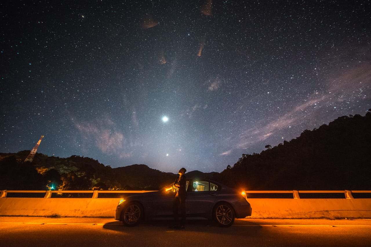夜里的水坝公路，钠灯把护栏照成橙色，Kevin 站在车旁，头顶是满天星斗。