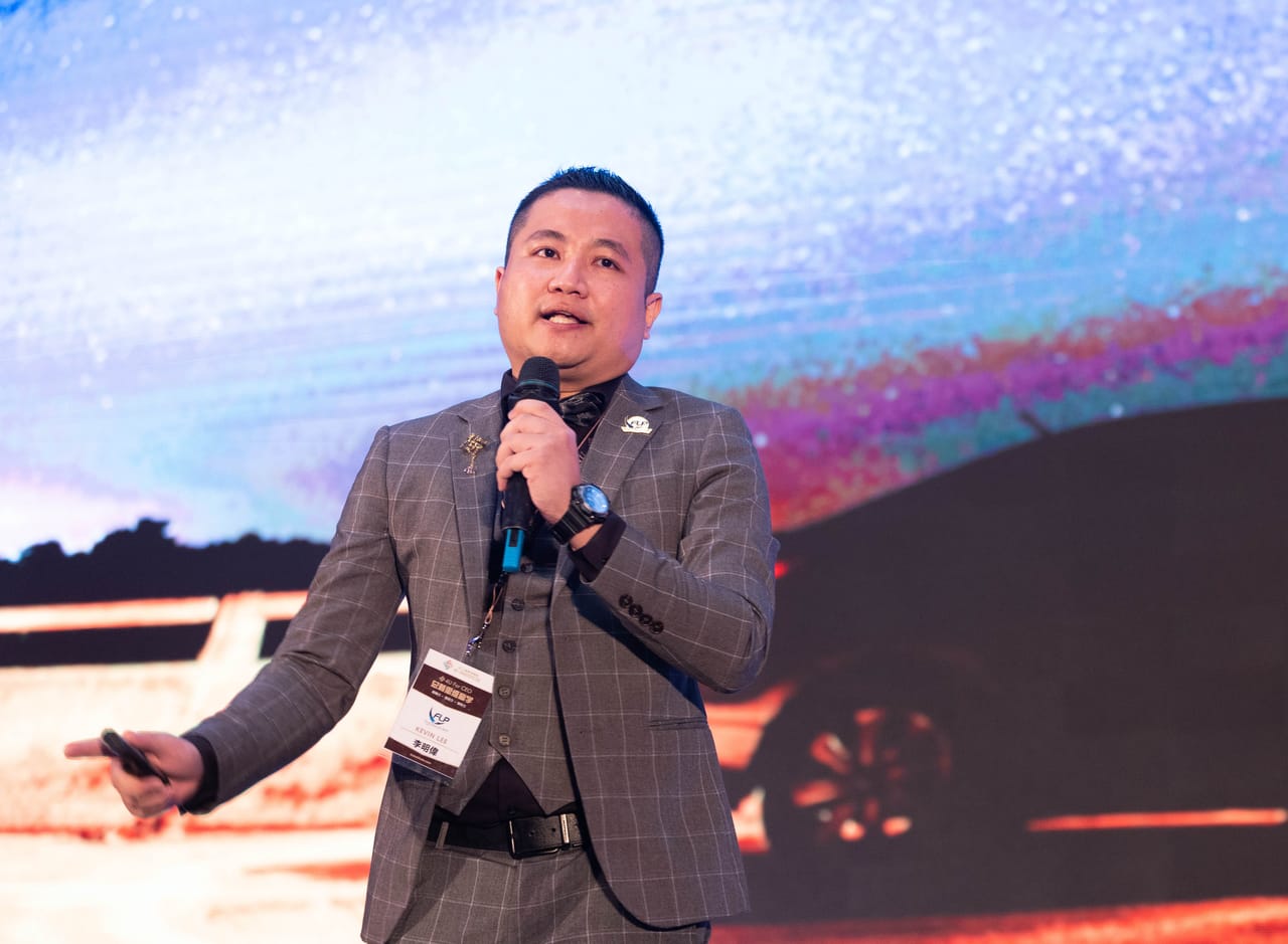 Kevin 拿着麦克风在台上分享，身后的大屏幕投影着他自己拍的银河自拍像。